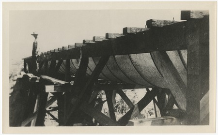 Man standing on trestle-supported steel pipe section of the San Diego flume