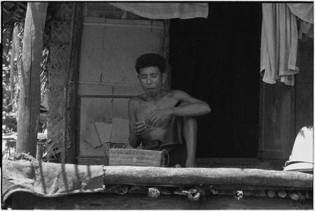 Man on veranda with a small basket, perhaps for betel nut