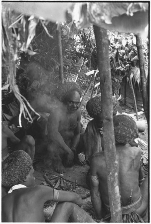 Pig festival, wig ritual, Tsembaga: men with red wigs under construction sit in shelter by men&#39;s house