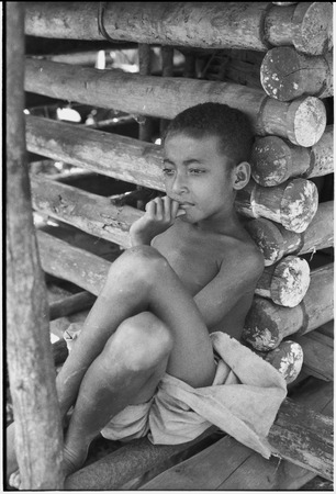 Boy leans against wall of a yam house, with good detail of notched pole construction