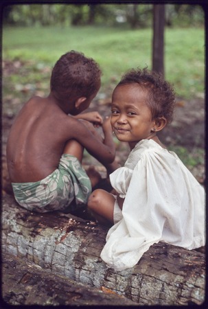 Children sitting on a log, Imala (r) smiles