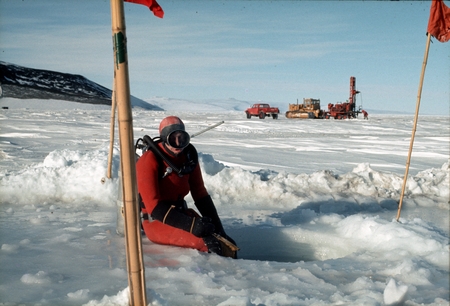 Diver at drilled hole through the sea ice in order to access the ocean below. Ice driller in background. McMurdo Station, ...
