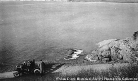 Man standing beside automobile on hill overlooking ocean along San Diego coast
