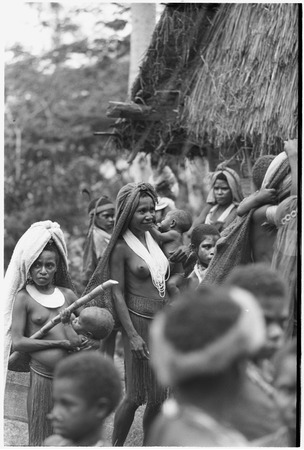 Pig festival, wig ritual, Tsembaga: women, several holding small infants, gather near dance ground to see wigged men emerge