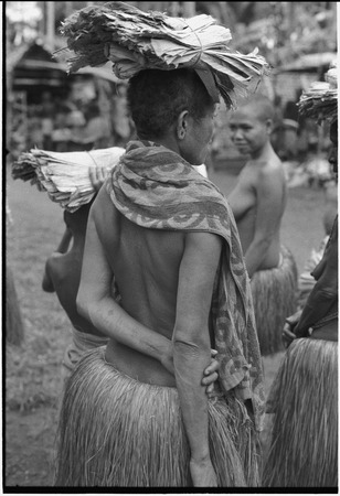 Mortuary ceremony, Omarakana: woman wears long fiber skirt, carries banana leaf bundles on head