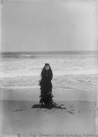 Woman standing on beach wrapped in seaweed to look like mermaid