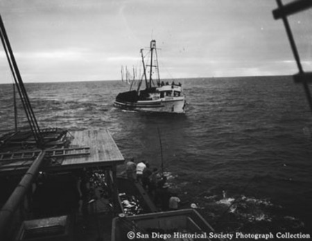 View looking astern of fishermen with bamboo poles and nearby tuna boat Zephyr
