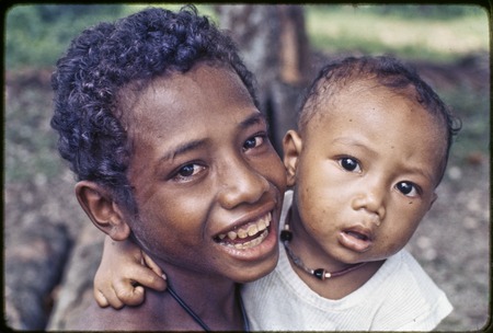 Smiling child and an infant wearing a shell necklace