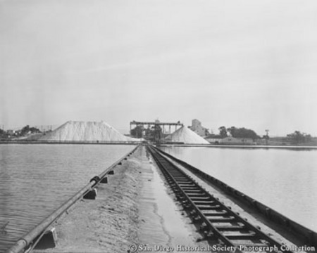 Railroad track running across saltwater reservoirs toward salt mounds and processing facility at Western Salt Company