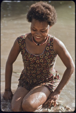 Young woman named Linette, wearing shell necklace and dress, splashing in shallow water