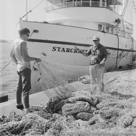 Two men handling fishing nets in front of docked tuna boat Starcrest