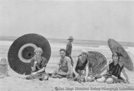 Man and three women in bathing suits with parasols sitting on San Diego beach