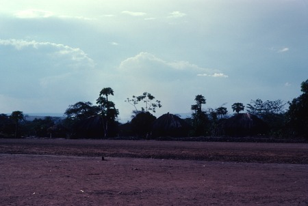 Main road into Kaputa village, from the east, with houses on the other side  of the road and the hills of the Democratic Republic of the Congo in the  background | Library