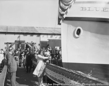 Woman preparing to break champaign bottle on bow of Bluefin during launching ceremony at Star and Crescent Boat Company