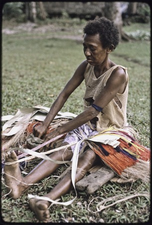 Weaving: woman makes colorful skirt from dyed banana fibers, tying them to cord stretched between her waist and foot
