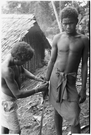 Man ties red cane obi on another man&#39;s wrist prior to a feast they are going to give.