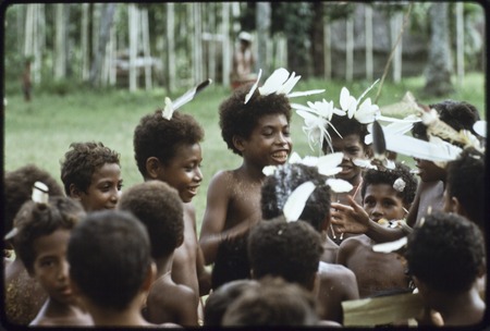 Dance: children, beautified with coconut oil and yellow pollen on skin, feathers and powder in hair, singing