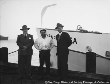 Three men posing on dock near bow of tuna boat Chicken of the Sea