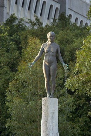 Standing: front view of bronze figure and upper part of concrete column