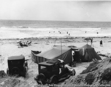 People wading in ocean surf and camping on Del Mar beach