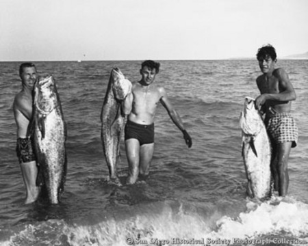 Three men in ocean surf holding tuna