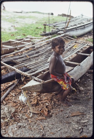 Canoes: Child sits on fishing canoe, other canoes in background at Wawela village