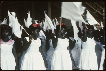 Girls dressed in white and holding white flags inside a building