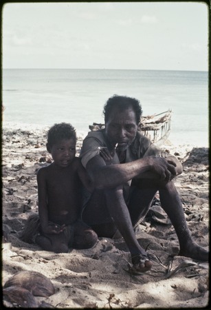 Smoking man sits with young girl on a beach near Kaibola village