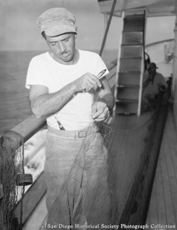 Fisherman mending net on boat