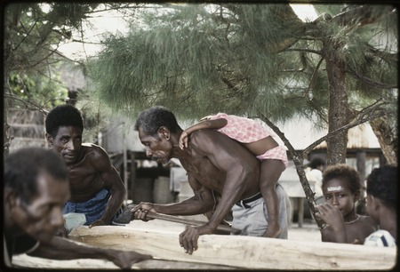 Manus: men building a canoe, small child on one man&#39;s back, Pere village