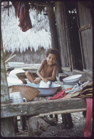 Domestic scene: child washes dishes in a basin on house veranda