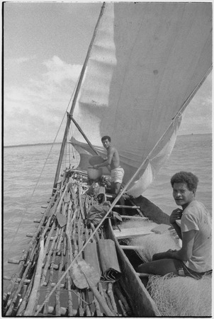 Canoes: men on outrigger canoe with sails up, paddles on platform, man (r)  sits on fishing net,, Library Digital Collections