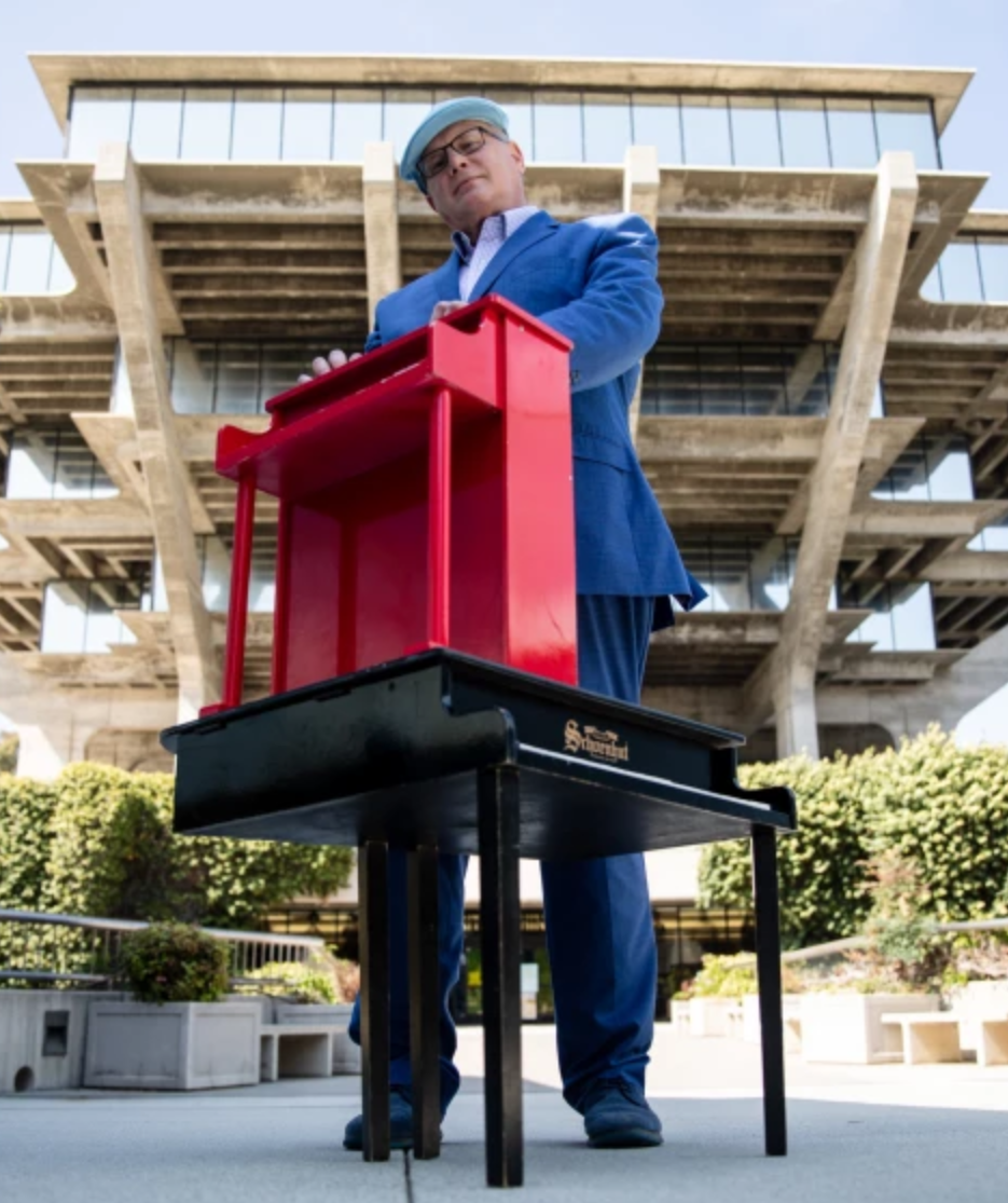 Portrait of Scott Paulson posed behind two small pianos and the Geisel Library Building in the background.