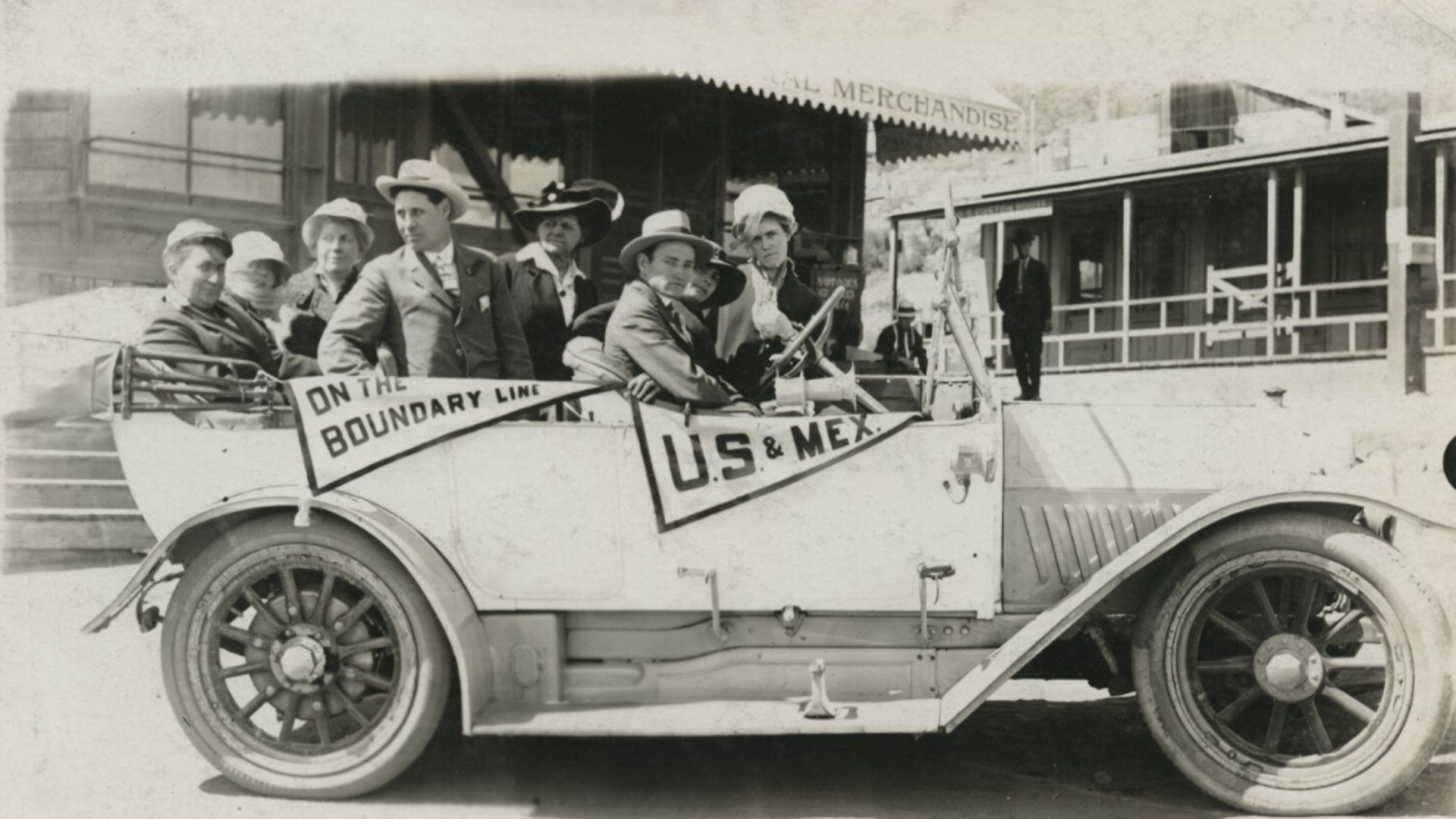 Automobile passengers with "On the boundary line" and "U.S. & Mex." pennants