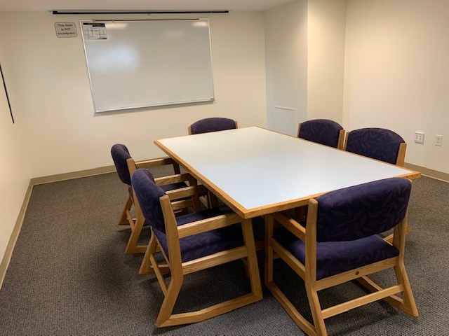 Long table with six purple chairs around it inside a room.