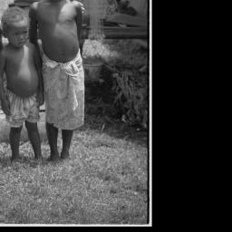 Adolescent girl wearing short fiber skirt stands with young girl in cloth  dress, both wear red shell necklaces, Library Digital Collections